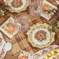 The Turkey & Gourds Table Setting Bundle by Sophistiplate LLC showcases Thanksgiving style with designer disposable plates adorned with turkey motifs, pumpkin-themed napkins, clear glasses, gold-trimmed utensils, and autumn floral centerpieces atop a plaid tablecloth.