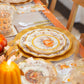 Create a festive autumn table with the Sophistiplate Turkey & Gourds Table Setting, featuring designer plates, gold utensils, elegant glassware, and pumpkin décor in warm orange, gold, and neutral tones.