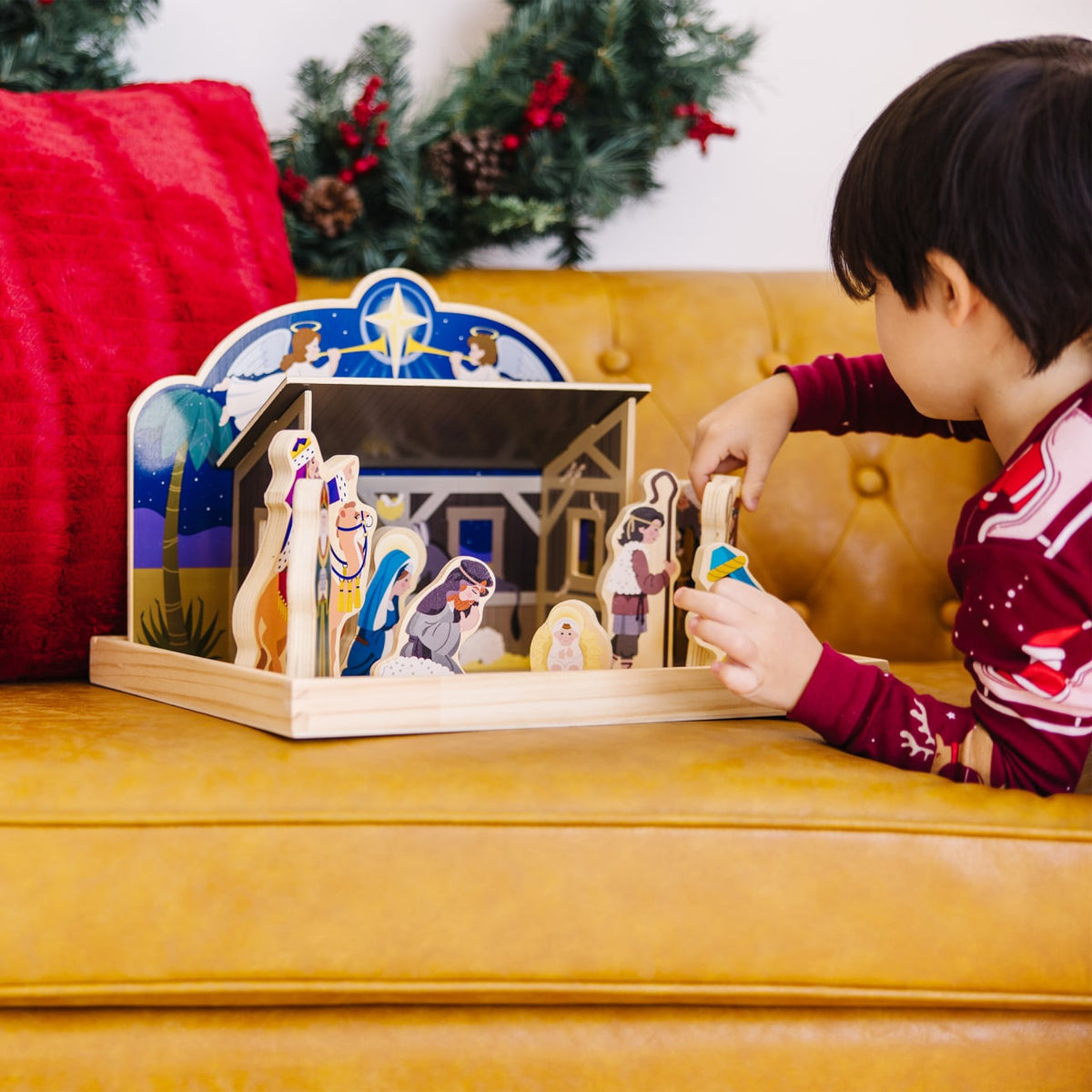 A kid playing with the Melissa & Doug Classic Wooden Christmas Nativity Set With 4-Piece Stable and 11 Wooden Figures